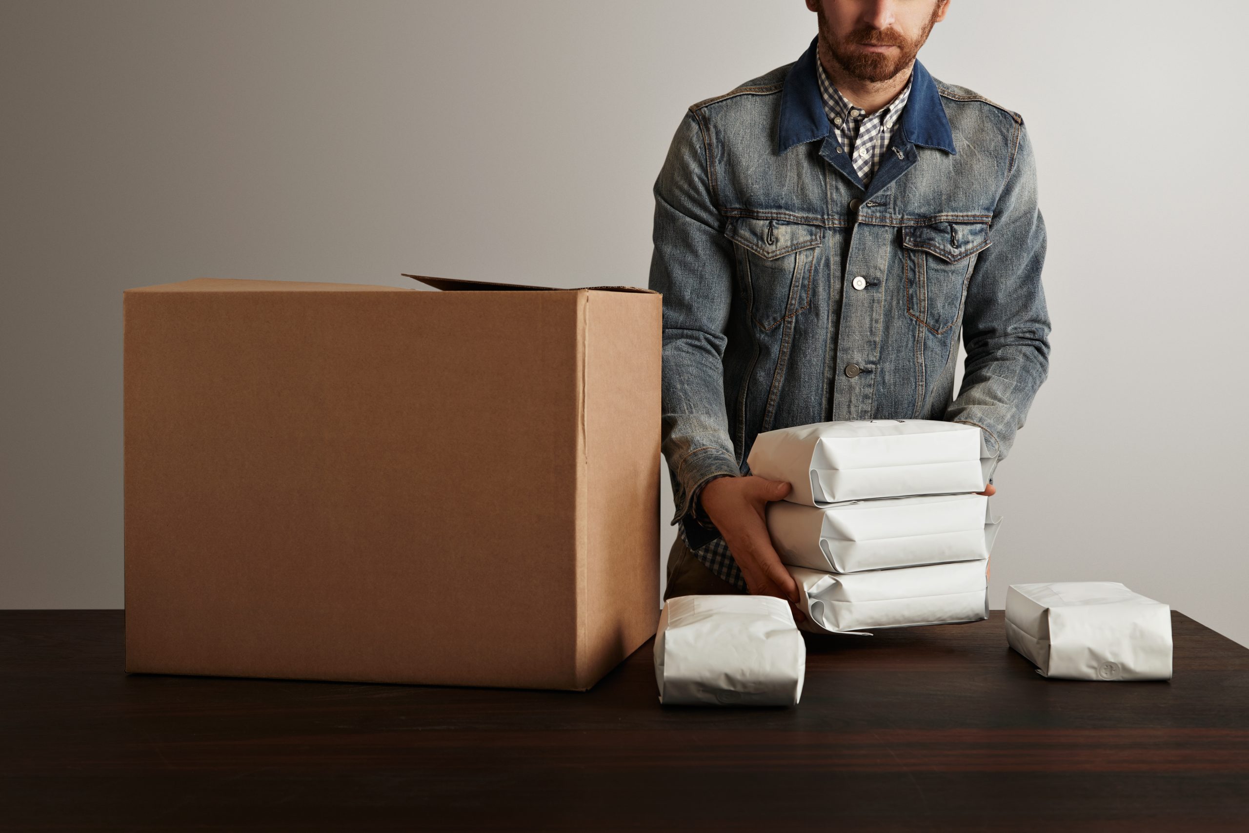 Man in work jacket placing sealed packages into a cardboard box for delivery